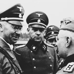 Heinrich Himmler voert overleg met SS-officieren tijdens een bezoek aan concentratiekamp Flossenbürg. Heinrich Himmler is links afgebeeld. Rechts van hem de kampcommandant Karl Künstler, rechts achter hem de adjudant Ludwig Baumgartner. Circa april 1940.