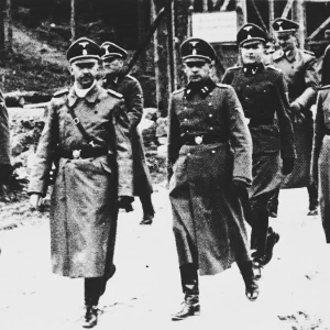 Heinrich Himmler op inspectieronde in het concentratiekamp Flossenbürg. Heinrich Himmler is afgebeeld als tweede van links. Rechts van hem de kampcommandant Karl Künstler, uiterst rechts de adjudant Ludwig Baumgartner. Op de achtergrond: Karl Wolff en Oswald Pohl (vanaf links). Circa april 1940.