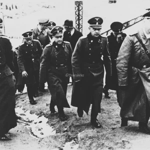 Heinrich Himmler inspecteert het concentratiekamp Flossenbürg. Heinrich Himmler is afgebeeld als tweede van rechts. Hij wordt vergezeld door zijn nieuwe adjudant Ludwig Baumgartner en Hans Hüttig, die verantwoordelijk was voor de kamppost en censuur. Ook afgebeeld is Schutzhaftlagerführer Hans Aumeier. 1940.