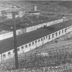 Zicht door het prikkeldraad op de gevangenenbarakken in concentratiekamp Flossenbürg. Flossenbürg, Duitsland, 1942.