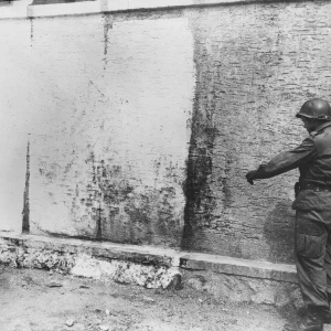 Muur waar slachtoffers in concentratiekamp Flossenbürg werden geëxecuteerd. Een soldaat van de 97ste Infanteriedivisie wijst naar bloedvlekken op de muur.
