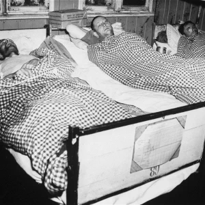 Drie overlevenden besmet met tyfus liggen in bedden in de ziekenbarakken van concentratiekamp Flossenbürg. Mei 1945